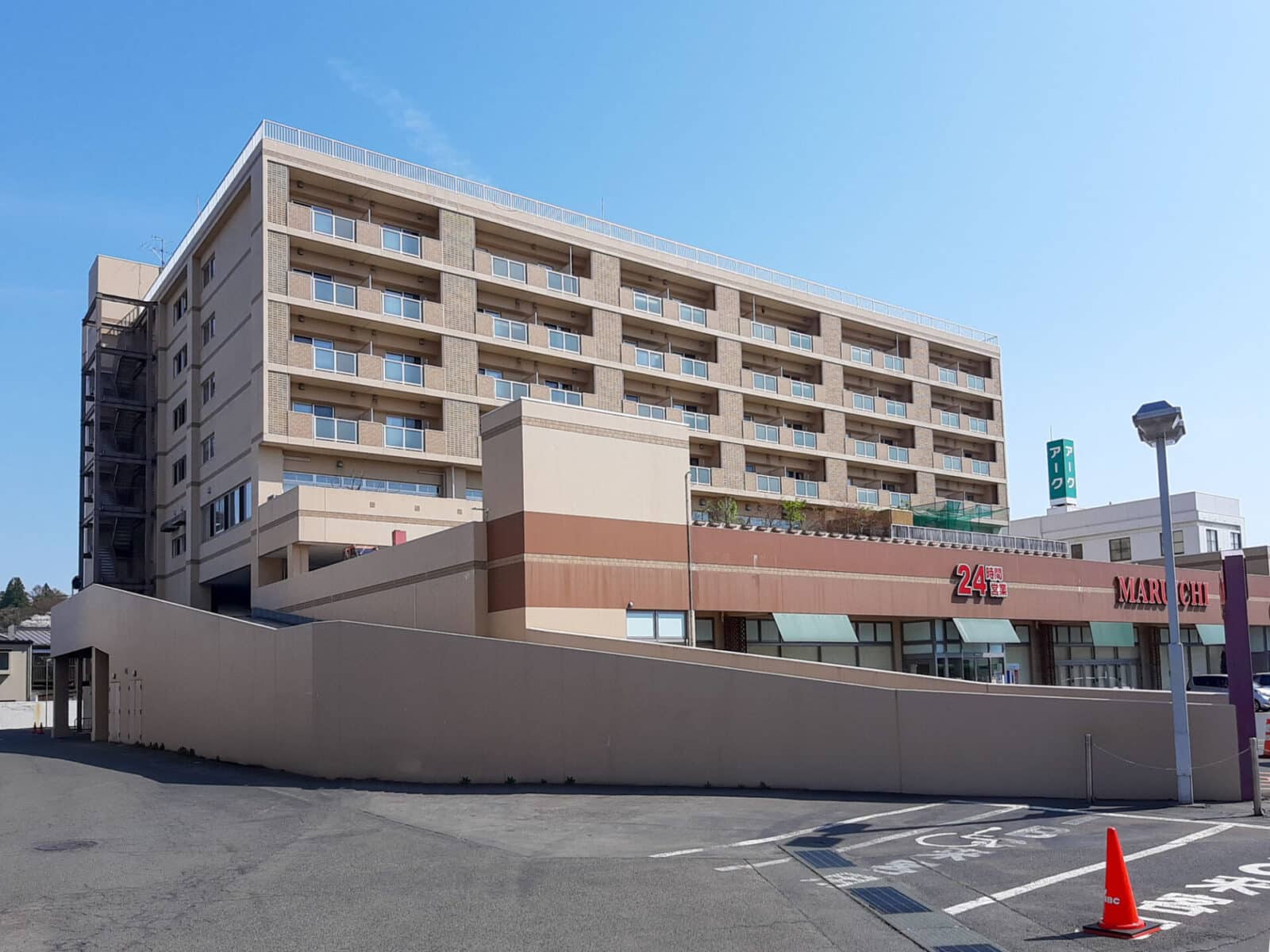 介護施設の建物外観。複数階建てで、ベージュと茶色のツートンカラーの外壁が特徴。晴天下での撮影。